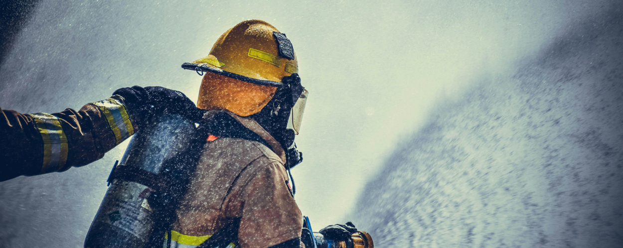 A brave firefighter in protective gear sprays water during training or emergency.