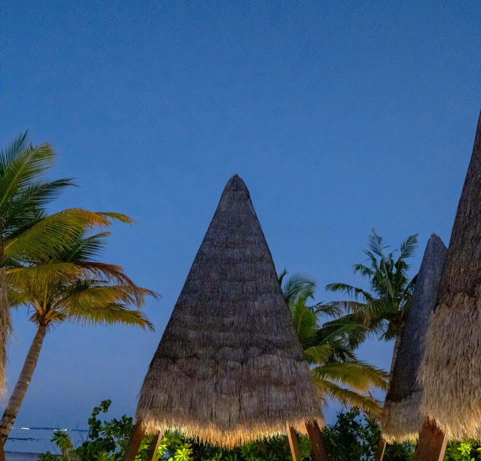 Charming tropical resort setting with huts and palm trees under a clear blue twilight sky.
